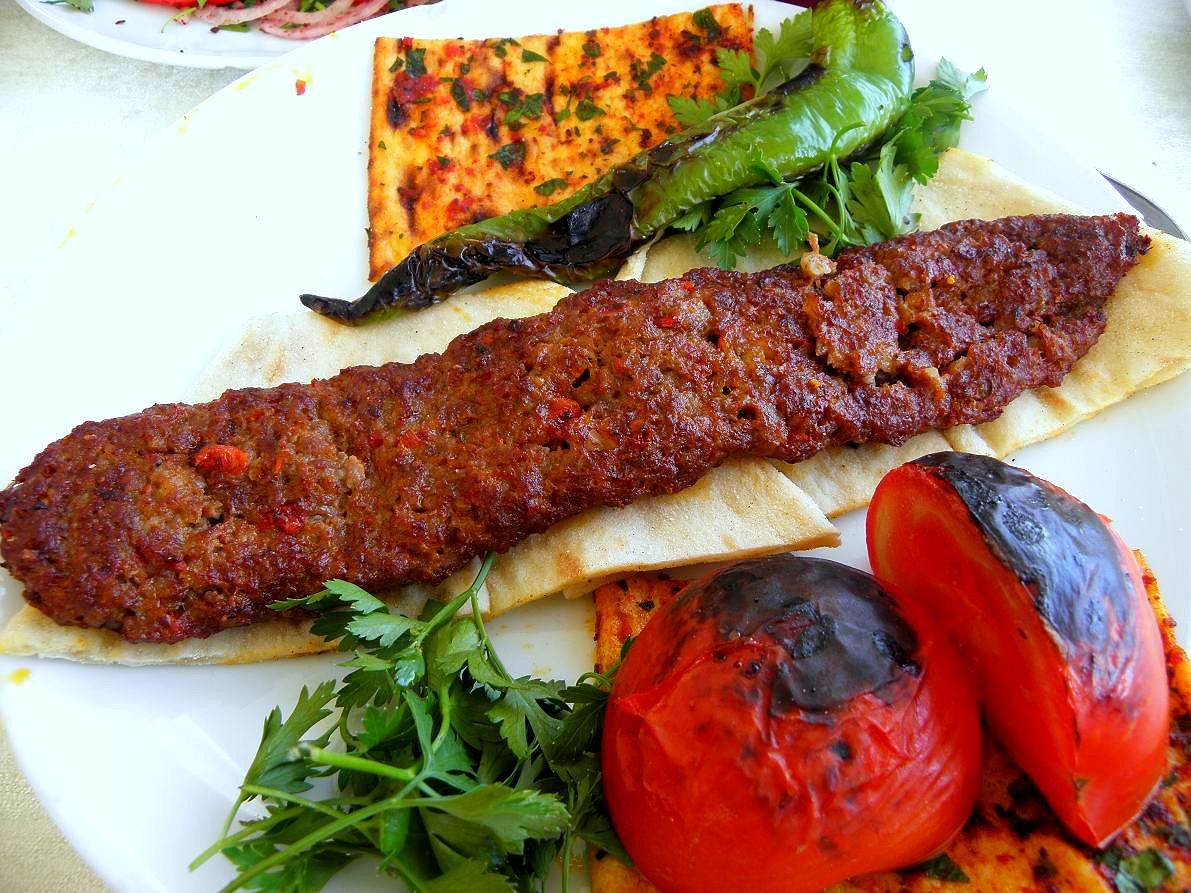 An Adana kebab served with grilled vegetables and flatbread