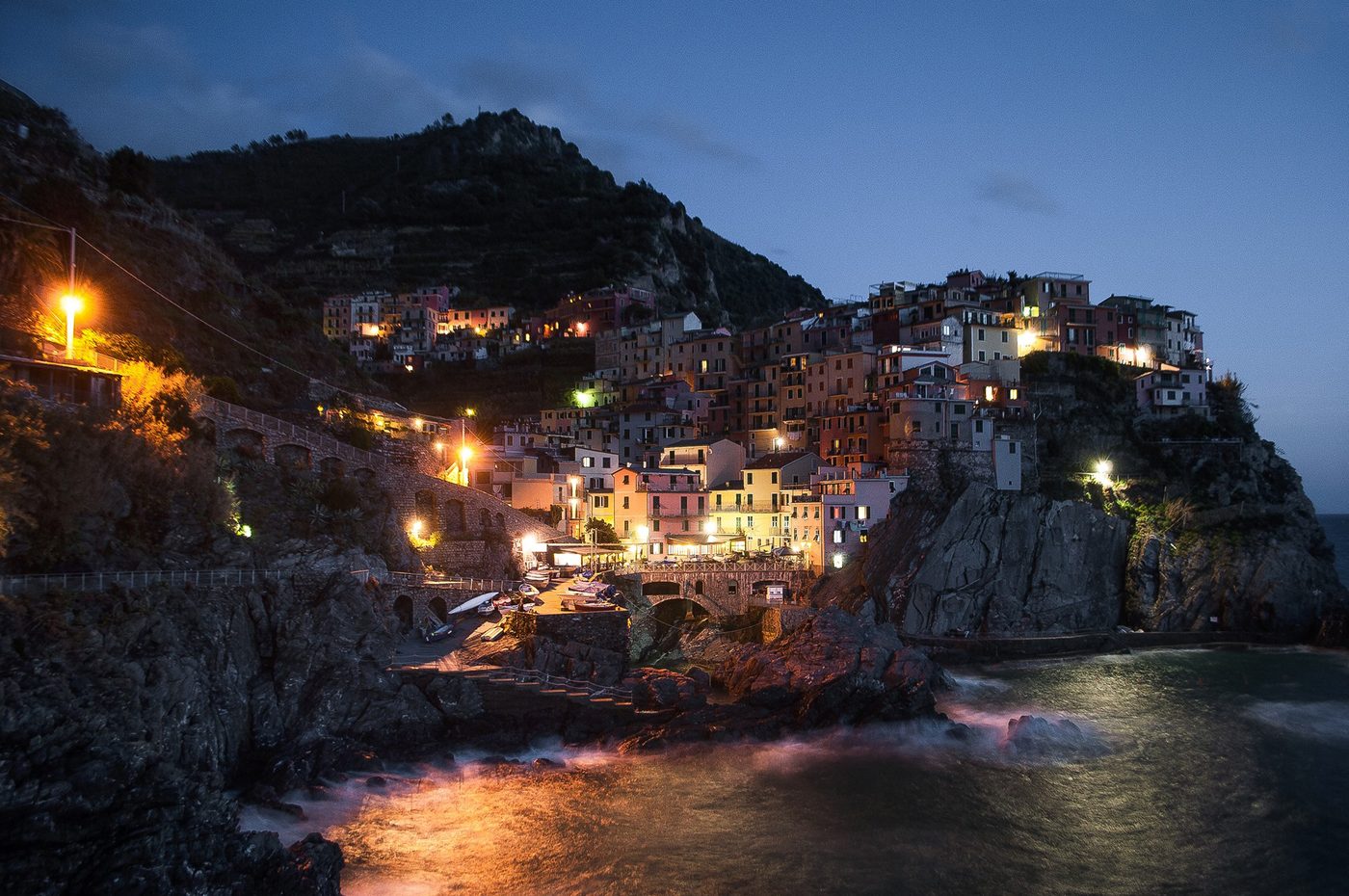 Manarola lit up at dusk above its harbour, the classic Cinque Terre sunset view