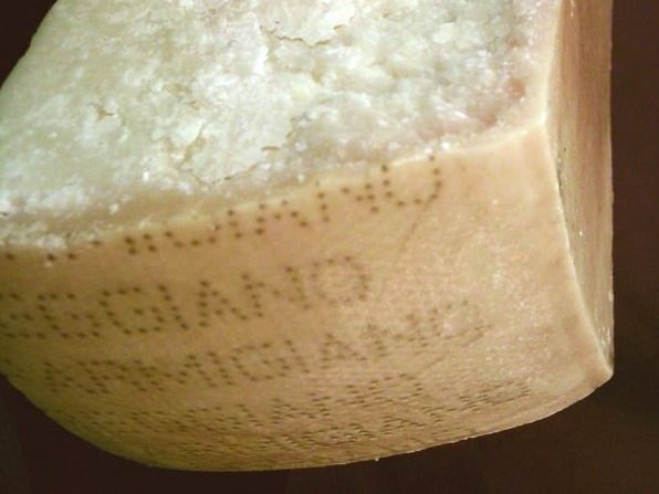 A wedge of Parmigiano Reggiano with the pin-dot lettering stamped into its rind